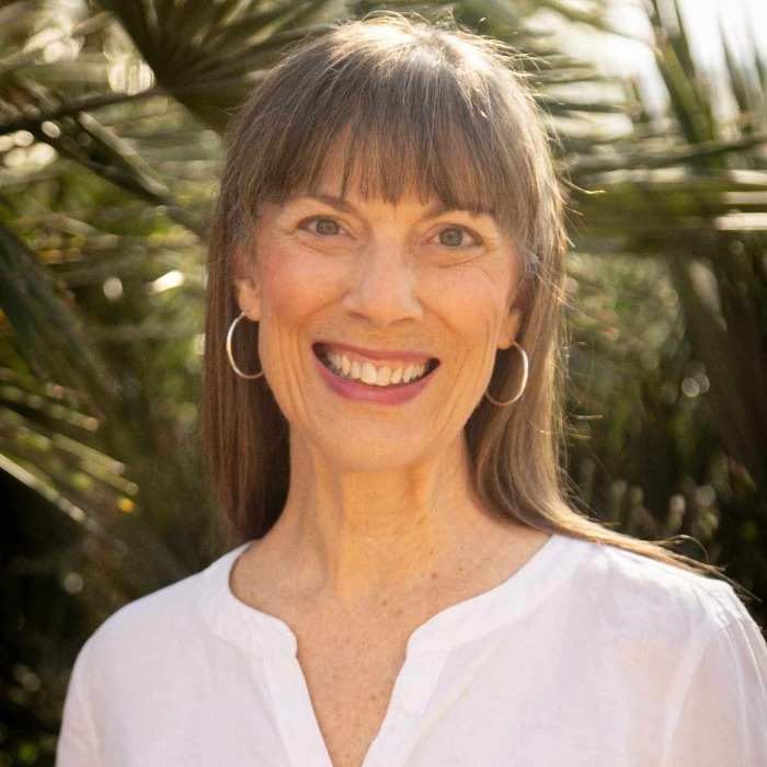 Smiling woman in white, radiating warmth, vitality, and balance in natural light.